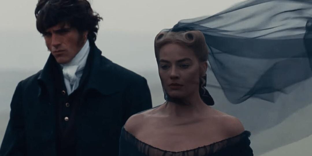 Homem e mulher em trajes de época caminham lado a lado em um cenário aberto e nublado; ela veste um vestido escuro com tecido esvoaçante ao vento, enquanto ele usa casaco preto e expressão séria, criando uma atmosfera melancólica e dramática.